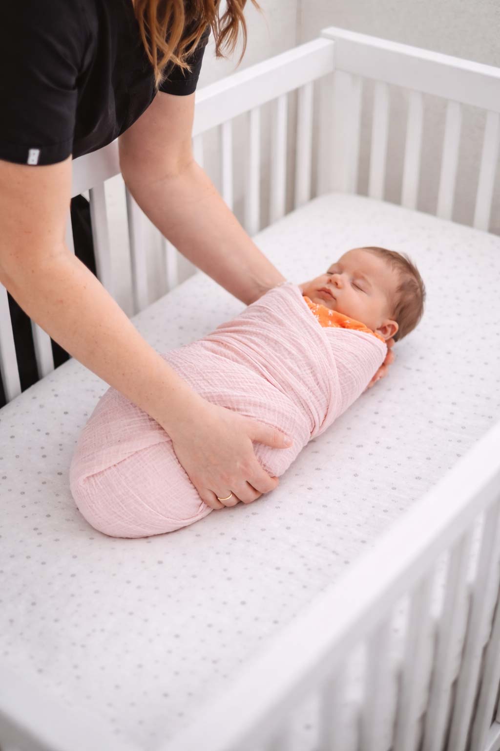 A nurse settling a swaddled baby onto a bare crib mattress with nothing else in the crib